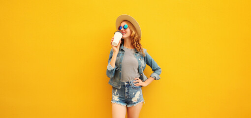 Beautiful stylish happy young woman with cup coffee wearing summer hat posing on yellow background