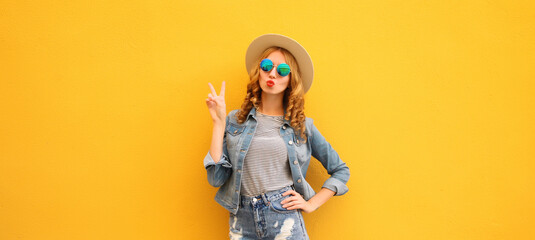 Portrait beautiful stylish young woman blowing kiss in summer hat posing on yellow studio background
