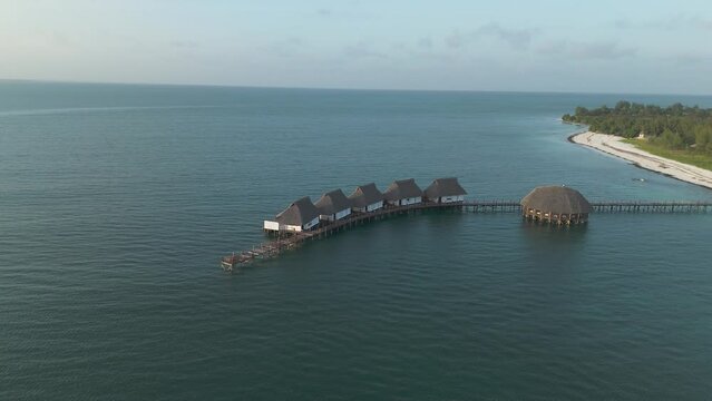 Aerial view orbiting luxurious thatched roof Kae Funk vacation lodges Indian ocean beach resort in Zanzibar Chwaka bay