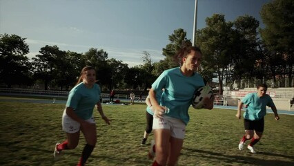 Intense Rugby Tackle During Women's Match - Female rugby players in red and blue jerseys engaged in an intense tackle, focusing on the rugby ball during a match. - Powered by Adobe