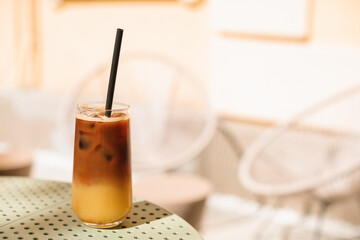 Iced coffee with pineapple juice in a glass with a straw on the table  on the summer terrace. Espresso, pineapple juice and syrup in layers.