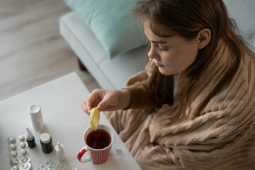 sick woman holding slice of lemon over cup of hot tea. treatment of flu, colds.