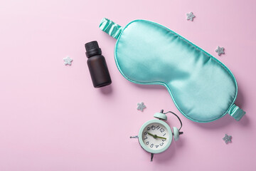 Sleep mask with essential oil, alarm clock, stars on pastel pink background, top view