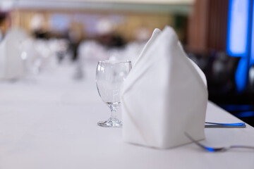 Close-up of a clear wine glass with a traditional round shape. On a white dining table with eating utensils, there is a blurry background of the restaurant