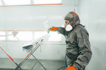 Auto painter painting a car with vaporizer gun inside a paint booth