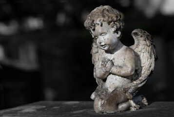 Close-up of a small old and weathered angel kneeling on a gravestone. There is space for text. The picture is monochrome