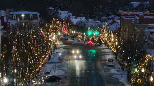 Christmas lights line Main Street in quaint American town during winter. Snow covered street with traffic at dawn.