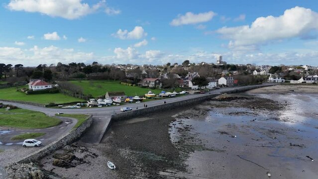 Reveal of southside of Bordeaux Harbour Guernsey at mid tide with harbour wall, boats on hardstanding,beach and cottages in the background on a bright day.