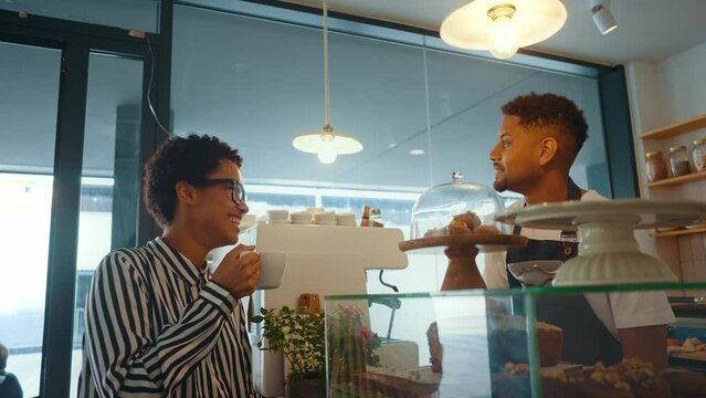 Cinematic image of waiters employees working in a nordic styled cafe. Waiter interact with a female customer. Client and barman conversating at the bar counter.
