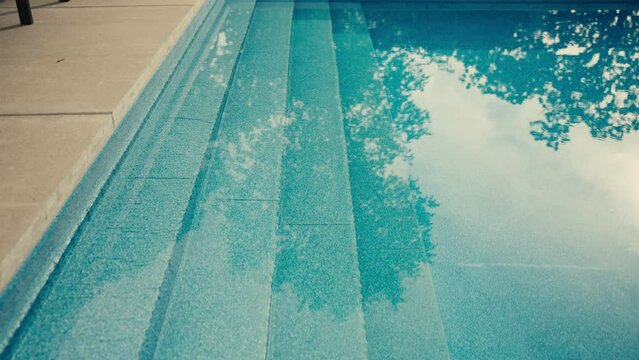 water and steps inside of a backyard pool with the reflection of trees and sunlight in the water