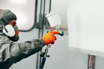Auto painter painting a car with vaporizer gun inside a paint booth