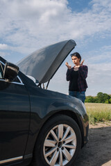 Young upset angry beautiful lonely female driver stands near a broken down black car after an...