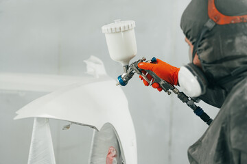 Auto painter painting a car with vaporizer gun inside a paint booth