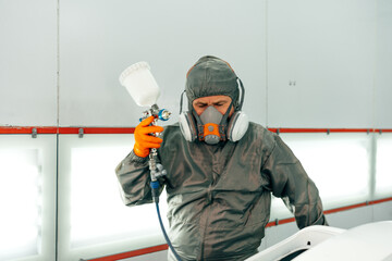 Auto mechanic worker wearing protective workwear spraying white paint on car part at workshop