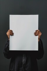 Person holding a blank white poster against a dark background.