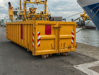 yellow steel open industrial waste container stands outside on the quay of the port
