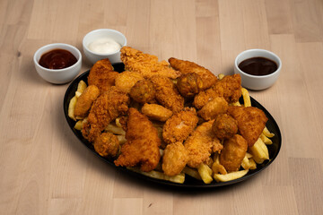 Close-up of chicken wings and fries served on a black plate with assorted dipping sauces