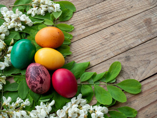 Close-up of vibrant Easter eggs with foliage and blooms on rustic wood
