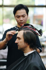 Barber trimming long hair of client with sharp scissors