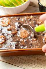 Close-up of traditional Brazilian feijoada in a pot being served, rich with black beans and sausages, perfect for a hearty meal.