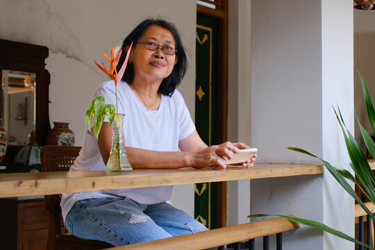 Asian woman sitting on high stool in her home veranda