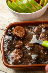 A traditional Brazilian feijoada, a savory black bean stew with sausage, served with fresh lime slices on the side.