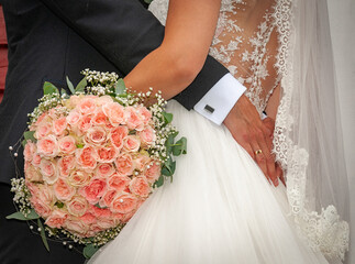 A bride and groom embrace, showcasing their love and commitment, with a stunning bouquet of pink...