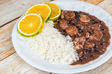 Delicious Brazilian feijoada served with white rice and fresh orange slices on a wooden table, a flavorful traditional dish.