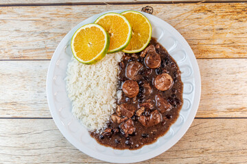 Traditional Brazilian feijoada served with white rice and sliced oranges on a rustic wooden table.