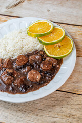 Top-down view of a traditional Brazilian feijoada with rice and orange slices served on a rustic wooden table.