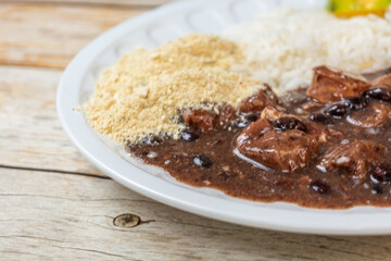 Close-up of a traditional Brazilian feijoada with black beans, meat, rice, and farofa, served on a white plate.