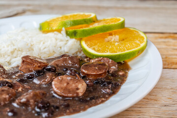 A delicious plate of Brazilian Feijoada served with rice, orange slices, and lime wedges on a rustic wooden table.