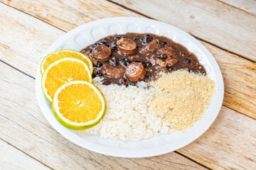 Traditional Brazilian feijoada served with rice, orange slices, and farofa on a rustic wooden table, showcasing a rich and hearty meal.