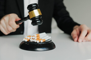 Judge hitting cigarettes with referee's gavel on white table. Tobacco law.
