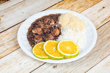 Traditional Brazilian feijoada served with orange slices, rice, and farofa on a rustic wooden table.