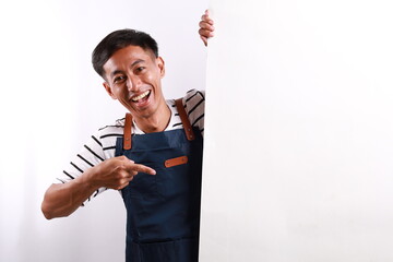 Cheerful Asian man in apron pointing something on white advertisement board on white background