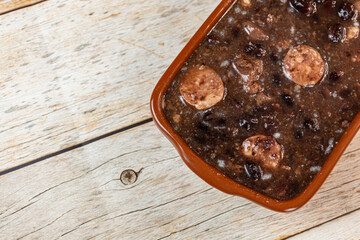 Traditional Brazilian feijoada stew with sausage and black beans served in an earthenware dish on a rustic wooden table.