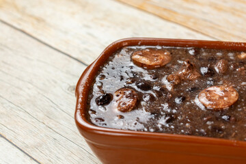 Traditional Brazilian feijoada served in a brown dish, showcasing a hearty stew with black beans, sausages, and aromatic spices on a rustic wooden table.