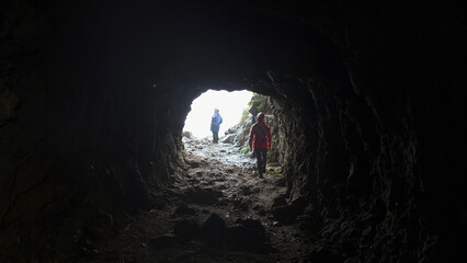 View from cave to tourists. Clip. Rear view of man coming out of cave. Tourist comes out of cave...