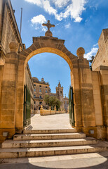 Scenic view through a medieval arched passage reveals the iconic Chapel of St. Mary Magdalene in Pjazza San Pawl Rabat historic core. Cultural heritage of Malta