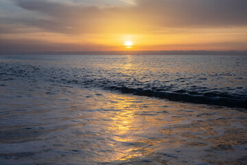 Fototapeta premium The sunset over the sea, with the sky tinged with gold and the light reflecting on the waters.