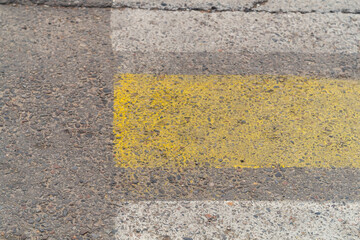 Fototapeta premium Edge of pedestrian crossing with strips of road reflective paint yellow and white colors, wear of the road surface and additional signals on the carriageway
