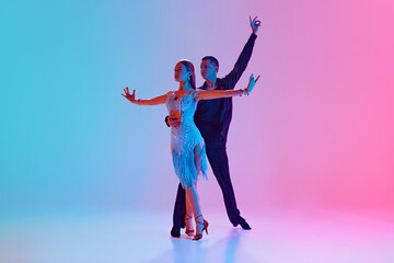 Duet of ballroom dancers, man and woman in festive costumes moving in neon lighting against gradient background. Concept of dance and music, professional sport, action, competition, classical. Ad