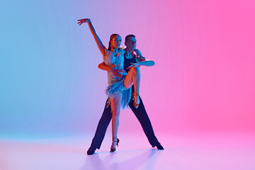 Dynamic portrait of elegant man and woman dressed stage costumes dancing ballroom dance in neon...