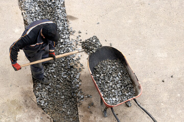 A worker pours gravel into a wheelbarrow.