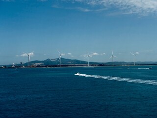 Fototapeta premium Boats sailing past windmills in the ocean beneath a clear blue sky