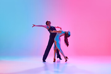 Two ballroom dancers in dramatic pose, male in black and female in shimmering dress in neon...