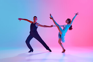 Male and female ballroom dancers captured mid-performance in neon lighting against gradient background. Concept of dance and music, professional sport, action, competition, classical. Ad