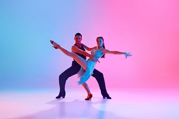 Portrait of young talented couple practicing ballroom dancing in motion in neon lighting against gradient background. Concept of dance and music, professional sport, action, competition, classical. Ad