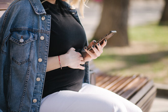 Middle selection of pregnant woman sits on bench in the park and using phone. Happy female have rest outdoor during the walks